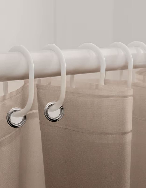 Closeup of beige striped shower curtain hanging on rod with hooks.